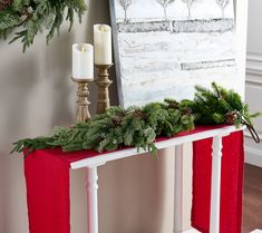 a christmas mantle with candles and greenery on it in front of a painting hanging on the wall