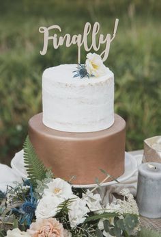 a wedding cake with flowers and greenery on the table next to it that says finally