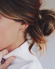 a close up of a woman wearing gold earrings and a white sweater with her hand on her neck