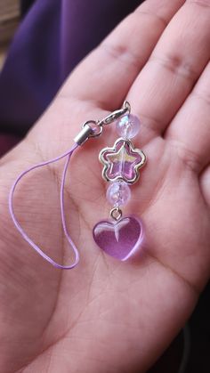 a hand holding a purple heart shaped glass beaded charm with a chain attached to it