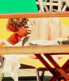 a man sitting on top of a beach chair next to a woman laying in the sun