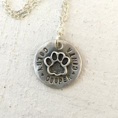 Pet memorial necklace This cat paw or dog paw necklace is a sweet reminder of your favorite pets. It also makes a lovely pet memorial necklace. The necklace can hold up to 22 characters/spaces combined. I can separate names with a tiny heart or a space.The only font I can use is the one shown in the photos and is available only in ALL UPPERCASE. The charm measures about 20mm across and the disc has hammered pattern. The photo shows it finished with a light matte/brush finish. But you can also op Hypoallergenic Sterling Silver Dog Tag Jewelry, Nickel-free Dog Tag Charm Necklace For Gift, Paw Print Round Pendant Jewelry For Gift, Paw Print Round Pendant Jewelry As Gift, Paw Print Round Pendant Jewelry Gift, Sterling Silver Paw Print Necklace For Gift, Adjustable Sterling Silver Paw Print Jewelry, Sterling Silver Paw Print Necklace As Gift, Small Personalized Sterling Silver Necklace