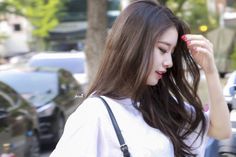 a woman with long brown hair is standing in front of parked cars and looking at her cell phone