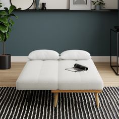 a white bed sitting on top of a wooden floor next to a potted plant