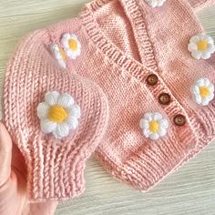 a pink sweater with white flowers on it and a hand in the foreground,