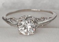 a white gold engagement ring with an intricate design on the band and a round diamond center stone