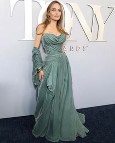 a woman in a green dress standing on a blue carpet with her hand on her hip