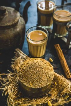 two cups filled with coffee next to cinnamon sticks and an old fashioned teapot on a table