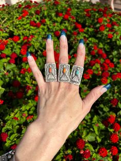 a woman's hand with two rings on it in front of some red flowers