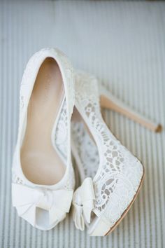 a pair of white shoes with bows on the toes and lace detailing are sitting on a bed