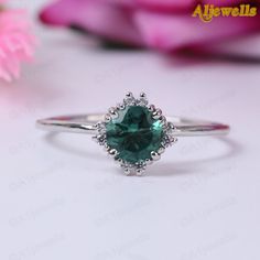 a close up of a ring with a green stone in the center and flowers behind it