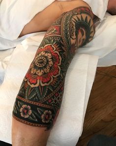 a man laying on top of a bed covered in white sheets and pillows with tattoos on his arm