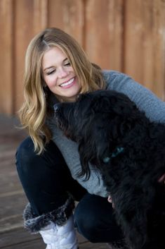 a woman holding a black dog on her lap and smiling at the camera while she is petting it