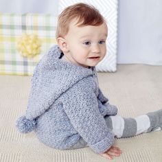 a baby sitting on the floor wearing a blue sweater