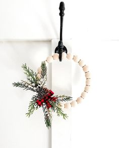 a wreath hanging on the side of a white door with a red ribbon and pine cones