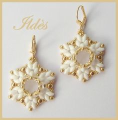 a pair of earrings with white flowers and gold beads on the ends, sitting next to each other