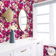 a bathroom with floral wallpaper and gold mirror above the sink, next to a window