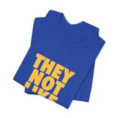 two blue t - shirts with the words they not in yellow letters on them, against a white background