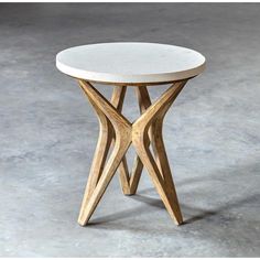 a white table with wooden legs and a circular top on concrete flooring area in front of grey wall