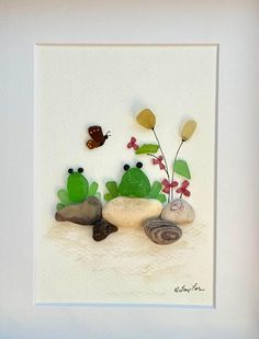 three frogs sitting on top of rocks with flowers in the middle and a butterfly flying over them