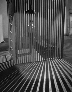 a black and white photo of a room with bars on the wall, light coming through