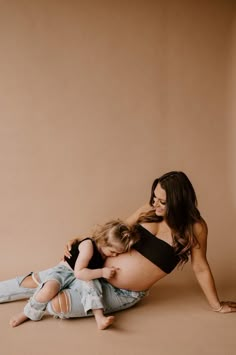 a pregnant woman and her child are sitting on the floor with their arms around each other