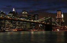 the city skyline is lit up at night as seen from across the water in new york