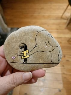 a person holding up a rock with an elephant and girl painted on it, in front of a wooden floor