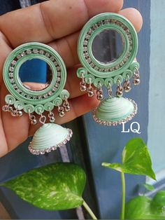 a pair of green earrings is shown in front of a potted plant and window