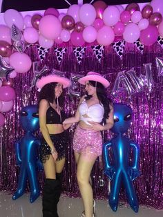 two women standing in front of balloons and streamers with pink hats on their heads