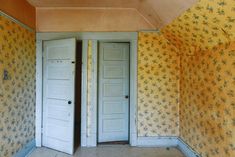 an empty room with two open doors and floral wallpaper on the walls behind it