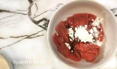 a bowl filled with meat and cheese on top of a marble counter next to a bottle of wine