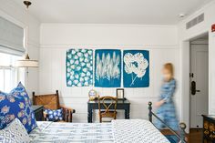 a bedroom with blue and white bedding, paintings on the wall and wooden furniture