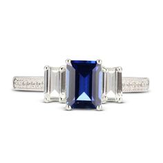 This sophisticated ring centers an emerald cut blue lab-created sapphire flanked on either side by an emerald-cut white lab-created sapphire. Round white lab-created sapphires sparkle down the gleaming sterling silver band to complete the elegant look. Rectangular Lab-created Sapphire Rings, Blue Rectangular Lab-created Sapphire Jewelry, Sapphire Square Cut Ring With Accent Stones, Blue Rectangular Lab-created Sapphire Rings, Blue Baguette Cut Emerald Ring, Lab-created Sapphire Three Stone Emerald Cut Rings, Blue Three Stone Emerald Cut Jewelry, Emerald Cut Sapphire Three Stone Jewelry, Blue Emerald Cut Three Stone Jewelry