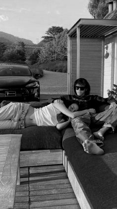 black and white photograph of two people laying on the back of a couch in front of a house