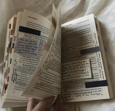 an open book with writing on it being held in someone's hand over a bed