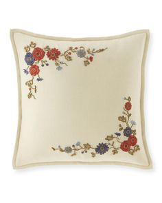 a white pillow with red, blue and green flowers on the front in an embroidered border