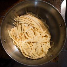 a large metal bowl filled with pasta on top of a table next to a stove