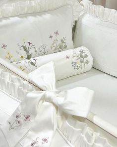 a bed with white sheets and flowers on it, next to a pillow that has a bow at the head