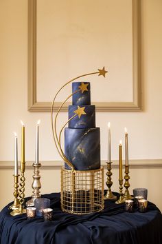 a blue and gold wedding cake with stars on the top is surrounded by silver candles