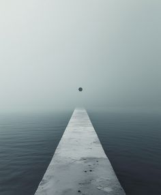 a long pier extending into the ocean on a foggy day with an object in the distance