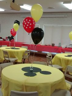 mickey mouse balloons are hanging from the ceiling at a party with yellow tablecloths