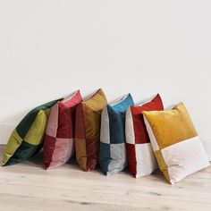 four different colored pillows lined up against a white wall in a row on the floor