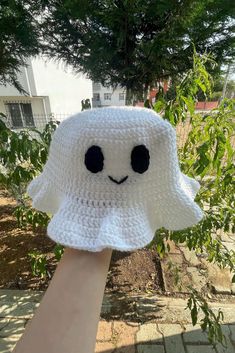 a hand holding up a white crocheted hat with black eyes and a smiling face