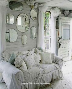 a living room filled with lots of white furniture and mirrors on the wall above it