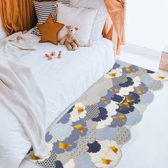 a white bed topped with lots of pillows next to a teddy bear on top of a rug