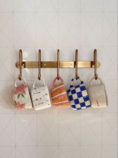 three mugs hanging on a rack in a kitchen with white tiles and gold handles