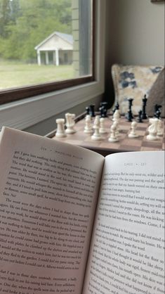 an open book sitting on top of a table next to a chess board and chair