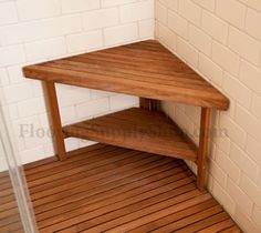 a corner wooden table sitting on top of a hard wood floor next to a white brick wall