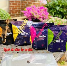 four bags of tea sitting on top of a table next to some plants and flowers